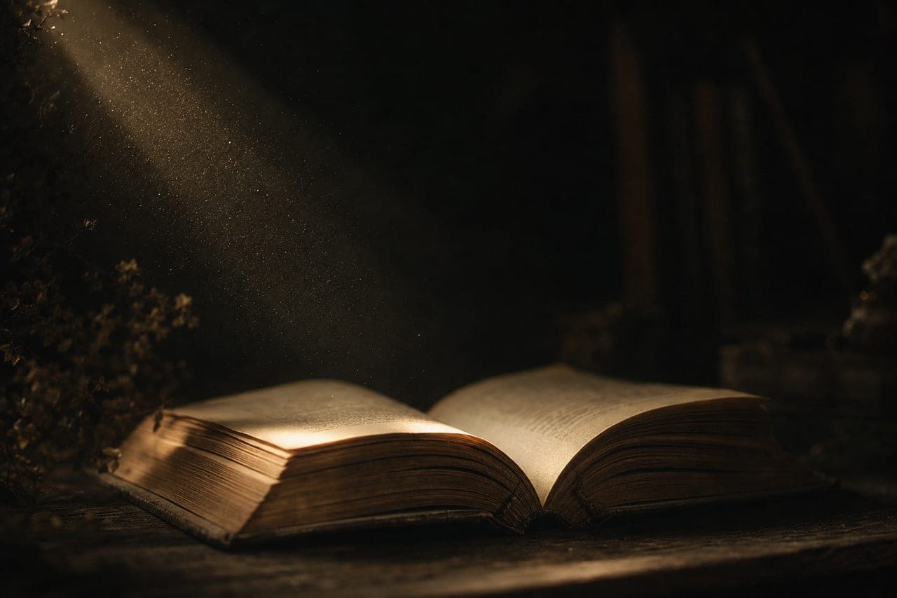 An open antique book catching a shaft of warm light in a dark room.
