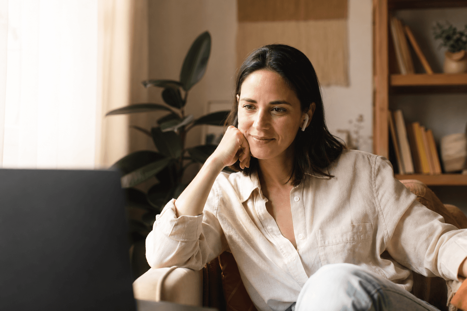 Warm editorial photograph of a person in a calm, sunlit room during a supportive telehealth therapy session